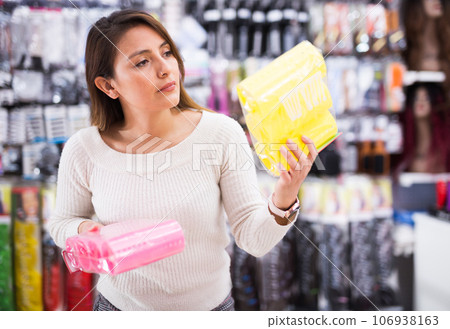 Young Latina choosing hair rollers in cosmetics store Young Latina choosing hair rollers in cosmetics store 106938163