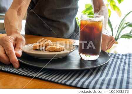 Person serving iced coffee and a plate of cookies to customers (at hand) 106938273
