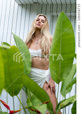 Beautiful young blonde woman in a top with long hair, natural beauty, daylight, in blue glasses, posing against the backdrop of a wooden fence and palm leaves 106938715