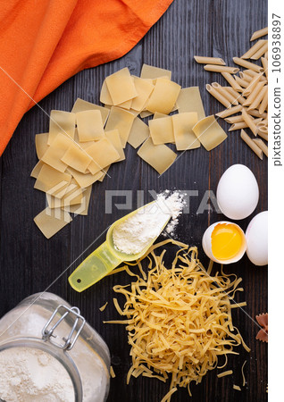 variety of types and shapes of italian pasta on dark wooden table with ingredients, flour and eggs. dry pasta background. flat lay 106938897