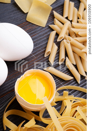 variety of types and shapes of italian pasta on dark wooden table with ingredients, flour and eggs. dry pasta background. close up 106938900