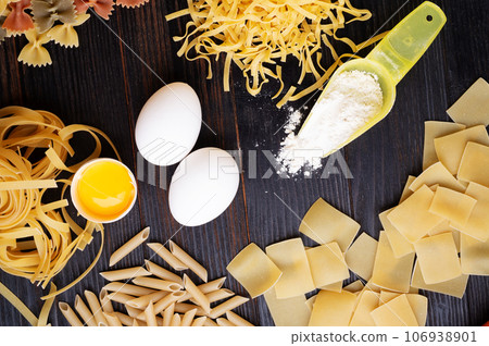 variety of types and shapes of italian pasta on dark wooden table with ingredients, flour and eggs. dry pasta background. flat lay 106938901