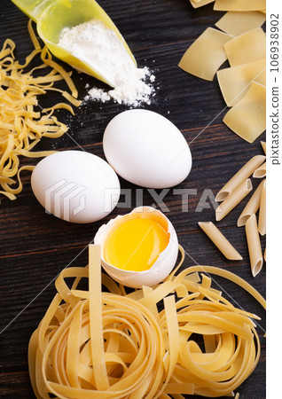 variety of types and shapes of italian pasta on dark wooden table with ingredients, flour and eggs. dry pasta background 106938902