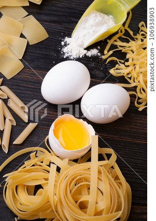 variety of types and shapes of italian pasta on dark wooden table with ingredients, flour and eggs. dry pasta background 106938903