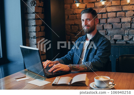 Handsome young man working on laptop while enjoying coffee in cafe Handsome young man working on laptop while enjoying coffee in cafe 106940258