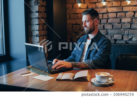 Handsome young man working on laptop while enjoying coffee in cafe 106940259