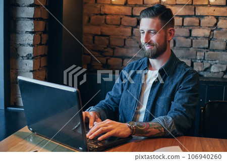 Handsome young man working on laptop while enjoying coffee in cafe Handsome young man working on laptop while enjoying coffee in cafe 106940260