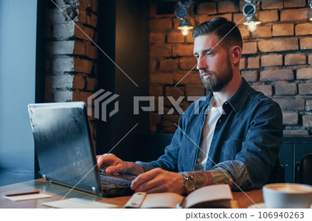 Handsome young man working on laptop while enjoying coffee in cafe 106940263