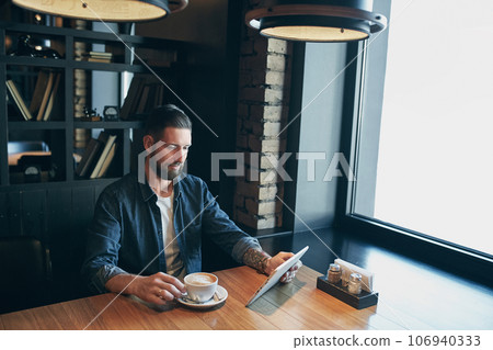 Young man drinking coffee in cafe and using tablet computer 106940333