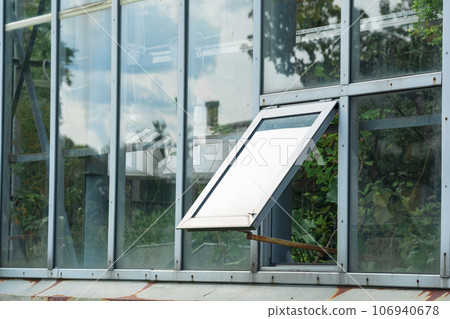 section of a glass wall of a tropical flower greenhouse with an open window, outside view 106940678