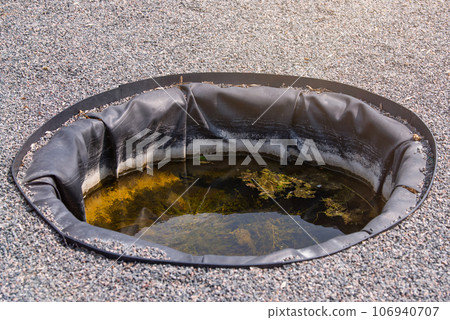 Container for watering plants in the garden. Artificial small pool in the garden for collecting rainwater and watering plants. 106940707