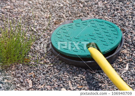 A plastic hatch in the garden covering the connection point for the irrigation hose. A protective hatch in the garden for connecting water and watering plants. 106940709