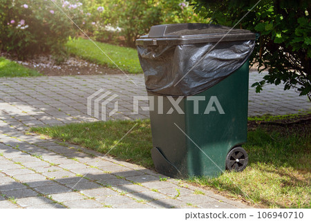 Close-up of a plastic trash can in a park. Garbage can on wheels, collecting and sorting waste in a park area. Container for collecting fallen leaves. 106940710