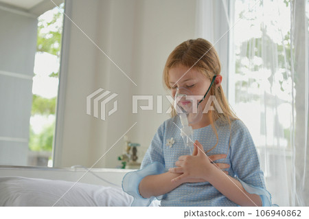 Caucasian girl having chest tightness in hospital room. She is using an oxygen concentrator to breathe. 106940862