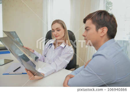 Doctor looking at x-ray results of patient in hospital. A patient is discussing test results with a doctor in the room. 106940866