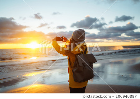 Tourist with phone. Selfie time. Tourist in yellow jacket posing by sea at sunset. Travelling. Tourist with phone. Selfie time. Tourist in yellow jacket posing by sea at sunset. Travelling. 106940887