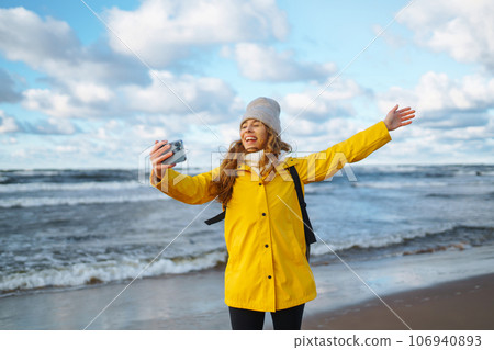 Tourist with phone. Selfie time. Tourist in yellow jacket posing by sea at sunset. Travelling. 106940893