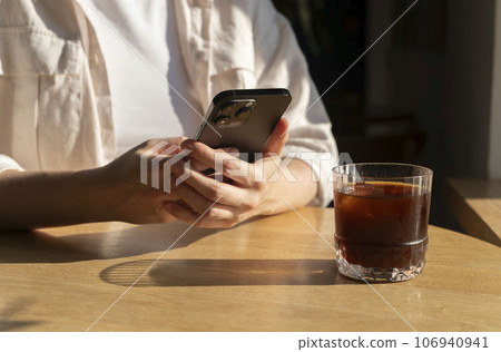 Berlin, Germany September 16 2023 Hands holding mobile phone, using smartphone at wooden table in coffee shop, cafe Berlin, Germany September 16 2023 Hands holding mobile phone, using smartphone at wooden table in coffee shop, cafe 106940941