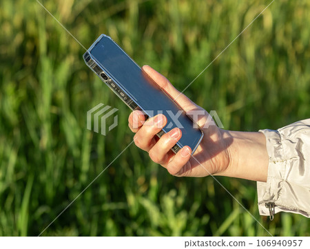 Hand holding mobile phone in nature, outdoors on green grass nature background Hand holding mobile phone in nature, outdoors on green grass nature background 106940957