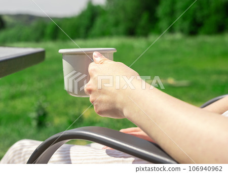Hand holding tea mug in nature, relaxing outdoors in summer Hand holding tea mug in nature, relaxing outdoors in summer 106940962