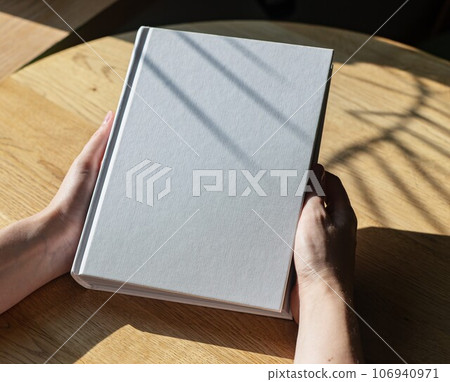 Hands holding closed book mockup on wooden table Hands holding closed book mockup on wooden table 106940971