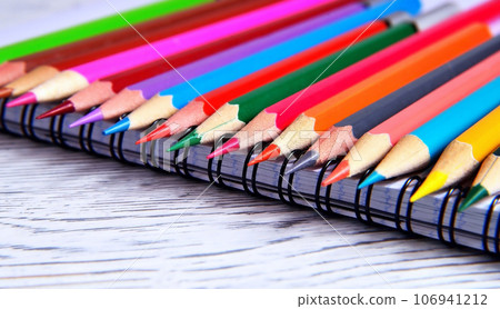 Color pencils lying on a pad with a spiral. Gray natural background, blur Color pencils lying on a pad with a spiral. Gray natural background, blur 106941212