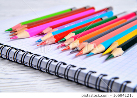 Color pencils lying on a pad with a spiral. Gray natural background, blur Color pencils lying on a pad with a spiral. Gray natural background, blur 106941213