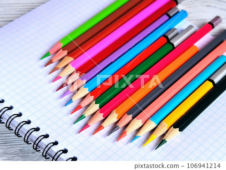 Color pencils lying on a pad with a spiral. Gray natural background, blur Color pencils lying on a pad with a spiral. Gray natural background, blur 106941214