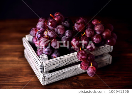 Branch of a dark grapes in a white box on a wooden background 106941396