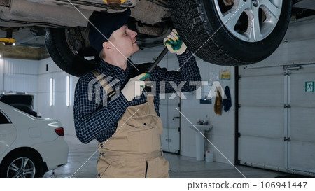 Auto mechanic inspects car suspension, car suspension diagnostics. Male mechanic inspecting a car Auto mechanic inspects car suspension, car suspension diagnostics. Male mechanic inspecting a car 106941447