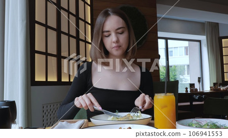 A young woman is having dinner in a restaurant, drinking orange juice and eating a steak. Beautiful Woman has lunch in a cafe, lunch in a restaurant. 106941553
