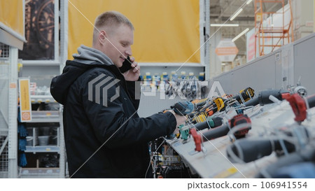 Buying a screwdriver at a hardware store. A man in a hardware store buys a power tool. Cordless power tools. Construction equipment supermarket 106941554