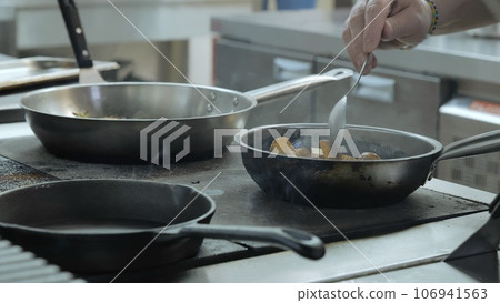 A professional chef prepares a gastronomic dish in a frying pan using ingredients and kitchen utensils. The chef is cooking in the kitchen of the restaurant The work of a cook in the kitchen. close-up A professional chef prepares a gastronomic dish in a frying pan using ingredients and kitchen utensils. The chef is cooking in the kitchen of the restaurant The work of a cook in the kitchen. close-up 106941563