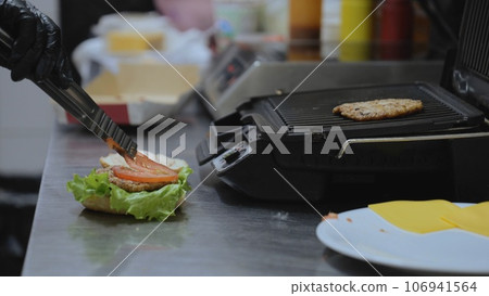 Cooking hamburger in the kitchen. Cooking a delicious burger. The chef puts onion rings while preparing a hamburger. Cooking hamburgers on a hot grill pan. Cooking hamburger in the kitchen. Cooking a delicious burger. The chef puts onion rings while preparing a hamburger. Cooking hamburgers on a hot grill pan. 106941564