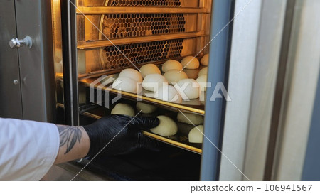 The cook puts the dough in the oven, baking oven, preparation for baking buns, a small oven for baking. The cook puts the dough in the oven, baking oven, preparation for baking buns, a small oven for baking. 106941567
