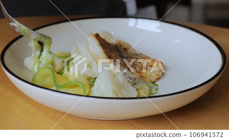 The male chef makes the composition of the dish for serving. The cook prepares a dish with fish. Close-up professional chef in the restaurant kitchen serving a dish adding the last ingredient 106941572