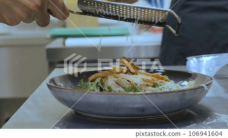The chef grates cheese on a grater on the finished dish, cheddar cheese is grated, the chef completes the dish, salad with shrimp and grated cheese, close-up The chef grates cheese on a grater on the finished dish, cheddar cheese is grated, the chef completes the dish, salad with shrimp and grated cheese, close-up 106941604