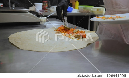 Shawarma in pita bread, shawarma pita vegetables fried potatoes cabbage onions, close-up of the process of cooking shawarma in pita bread, cooking tongs put vegetables on pita bread. Shawarma in pita bread, shawarma pita vegetables fried potatoes cabbage onions, close-up of the process of cooking shawarma in pita bread, cooking tongs put vegetables on pita bread. 106941606