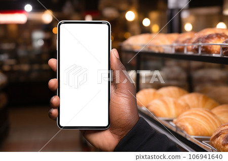 African man hand holding smartphone in bakery shop. smartphone with empty white display mockup. 106941640