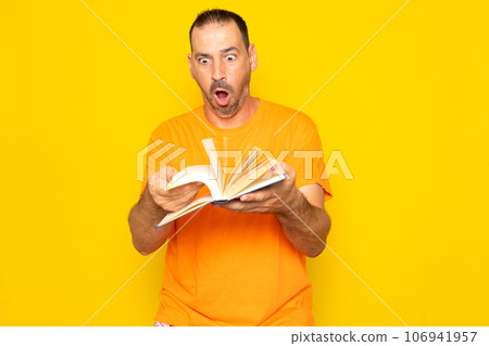 Bearded Hispanic man in his 40s turning the pages of a book visibly excited, isolated on yellow studio background. Bearded Hispanic man in his 40s turning the pages of a book visibly excited, isolated on yellow studio background. 106941957