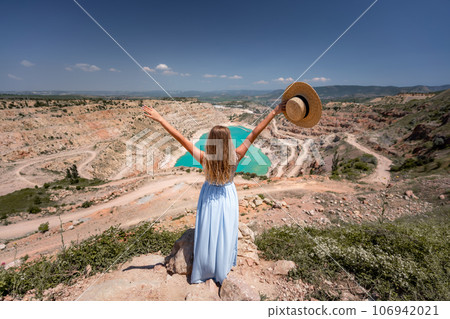 Portrait of a young woman on the beach by the sea, sitting with raised hands in a white dress and hat. Back photo 106942021