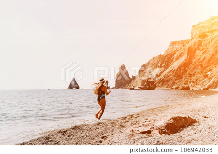 Woman travel summer sea. A happy tourist in a blue bikini enjoying the scenic view of the sea and volcanic mountains while taking pictures to capture the memories of her travel adventure. 106942033