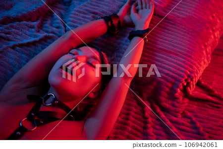 portrait of a sexy girl in a leather mask and bdsm accessories on a bed enjoying sex in orgasm with emotions on her face in neon light portrait of a sexy girl in a leather mask and bdsm accessories on a bed enjoying sex in orgasm with emotions on her face in neon light 106942061