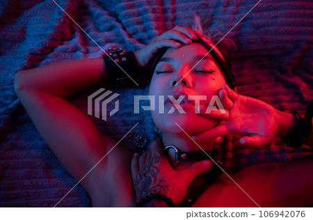 portrait of a sexy girl in a leather mask and bdsm accessories on a bed enjoying sex in orgasm with emotions on her face in neon light portrait of a sexy girl in a leather mask and bdsm accessories on a bed enjoying sex in orgasm with emotions on her face in neon light 106942076