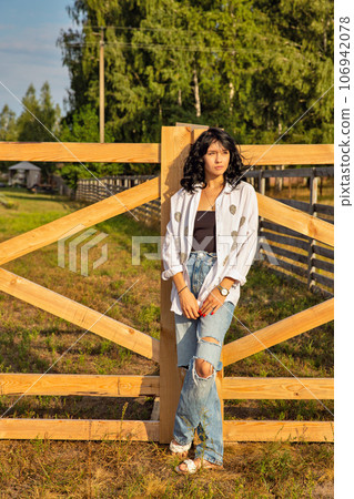Beautiful young caucasian woman standing at the ranch gate. 106942078