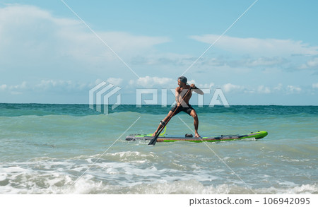 athletic wiry surfer guy swims with a paddle on a sapboard in the sea athletic wiry surfer guy swims with a paddle on a sapboard in the sea 106942095