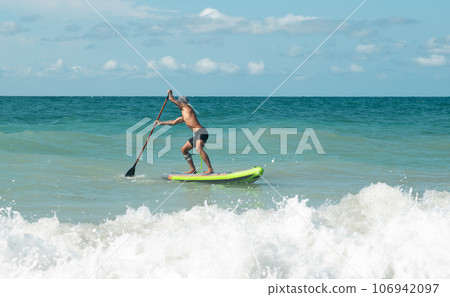 athletic wiry surfer guy swims with a paddle on a sapboard in the sea 106942097