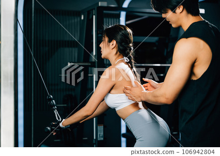 Personal trainer guiding a client through a weight training session, using a pull-down machine to work on the muscles of the upper body, GYM healthy lifestyle concept 106942804