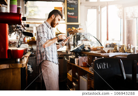 Digital tablet, research and cafe owner working on a startup cafeteria business plan in a restaurant. Technology, entrepreneur and male barista or waiter checking stock on a mobile in his coffee shop Digital tablet, research and cafe owner working on a startup cafeteria business plan in a restaurant. Technology, entrepreneur and male barista or waiter checking stock on a mobile in his coffee shop 106943288