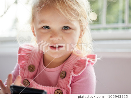 Can I play games. a little girl using a phone at home. 106943325